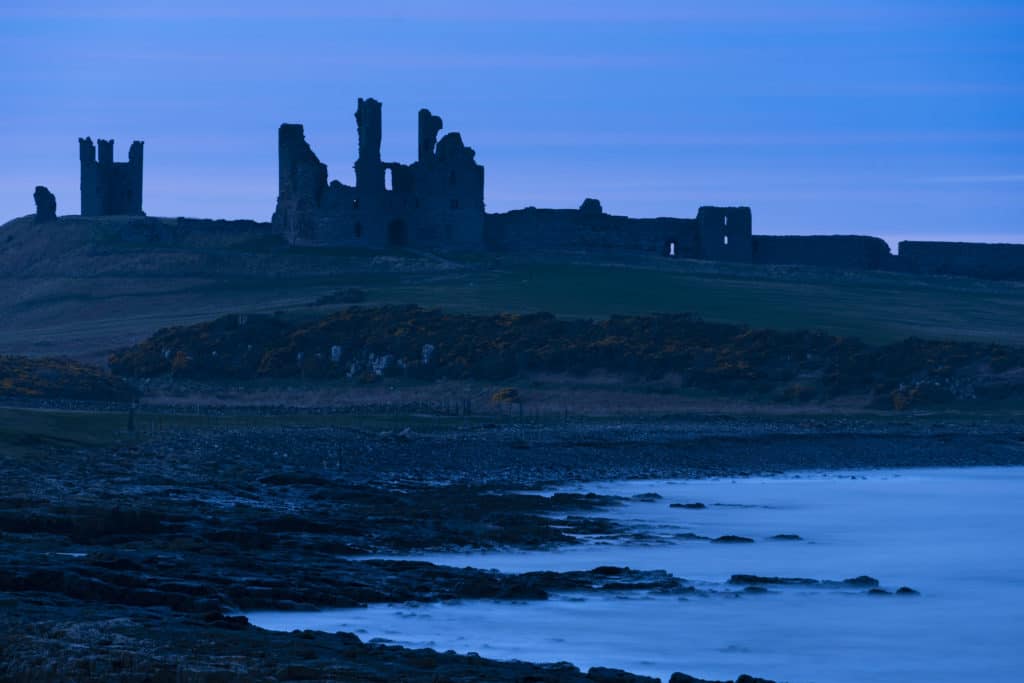 Dunstanburgh Castle on top of hill near body of water